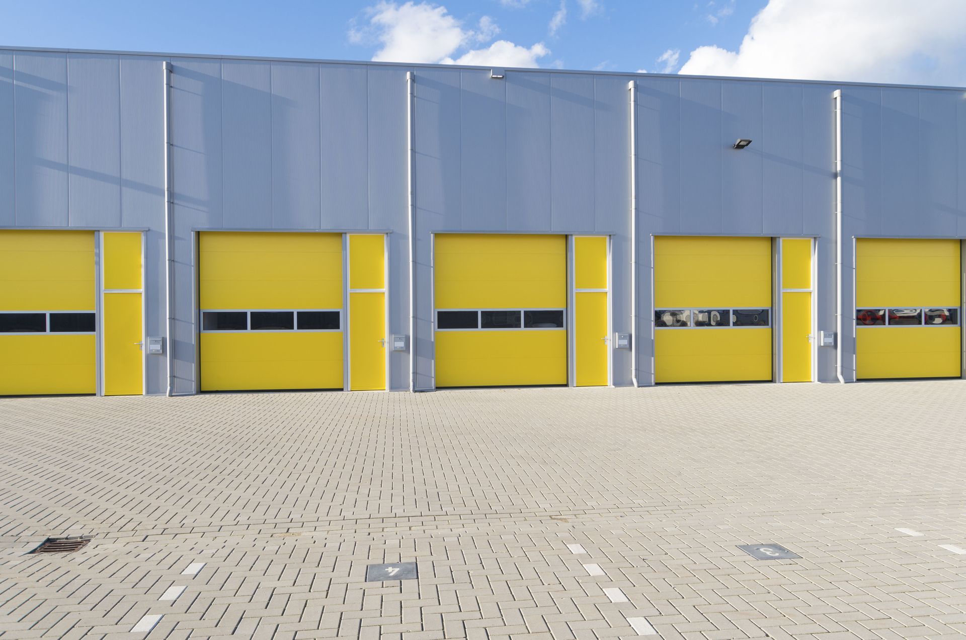 Modern industrial building with yellow loading bay doors and a paved foreground under a blue sky