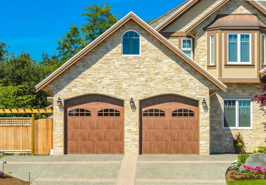 A house with a stone-front two-car garage and tan siding under a bright blue sky