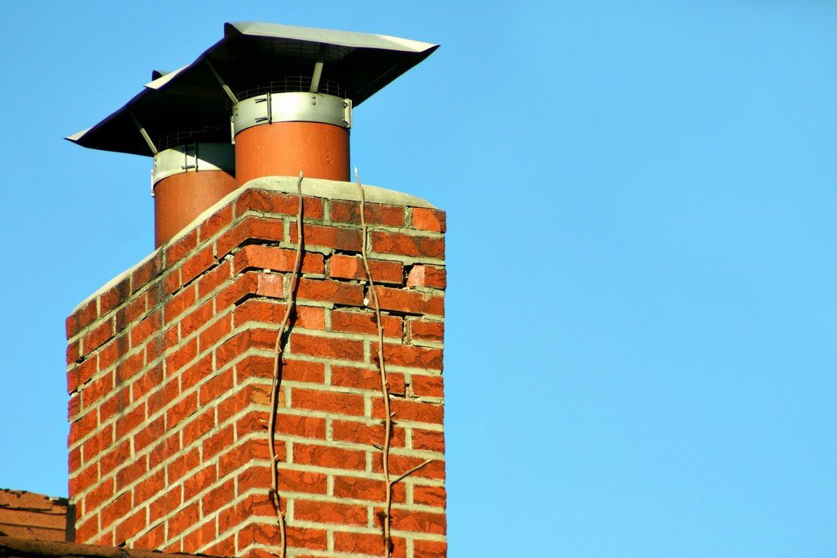 A brick chimney with two metal flue caps against a bright blue sky.