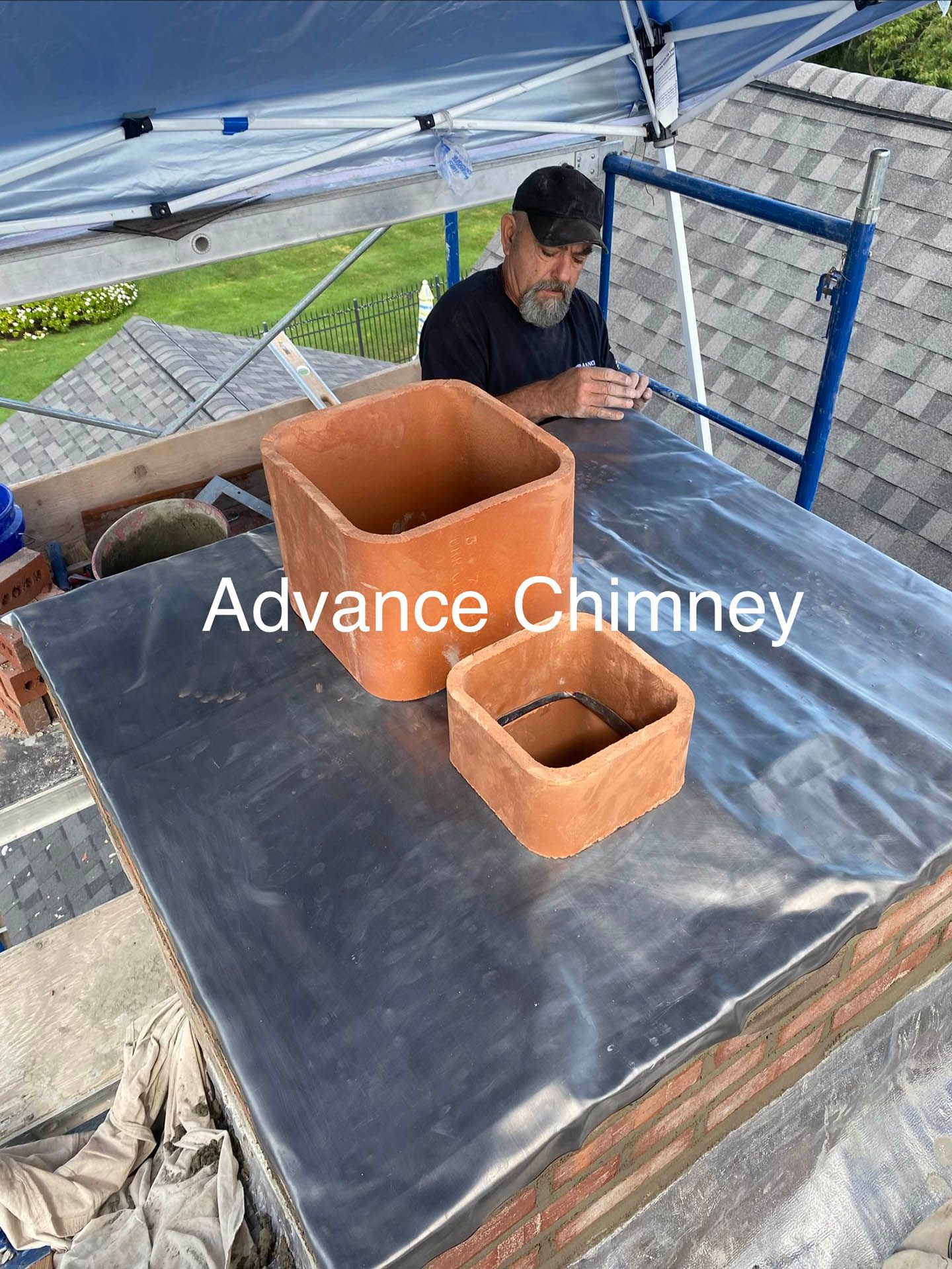 A technician installs two terracotta chimney flue liners onto a rooftop covered with a protective membrane under a canopy.