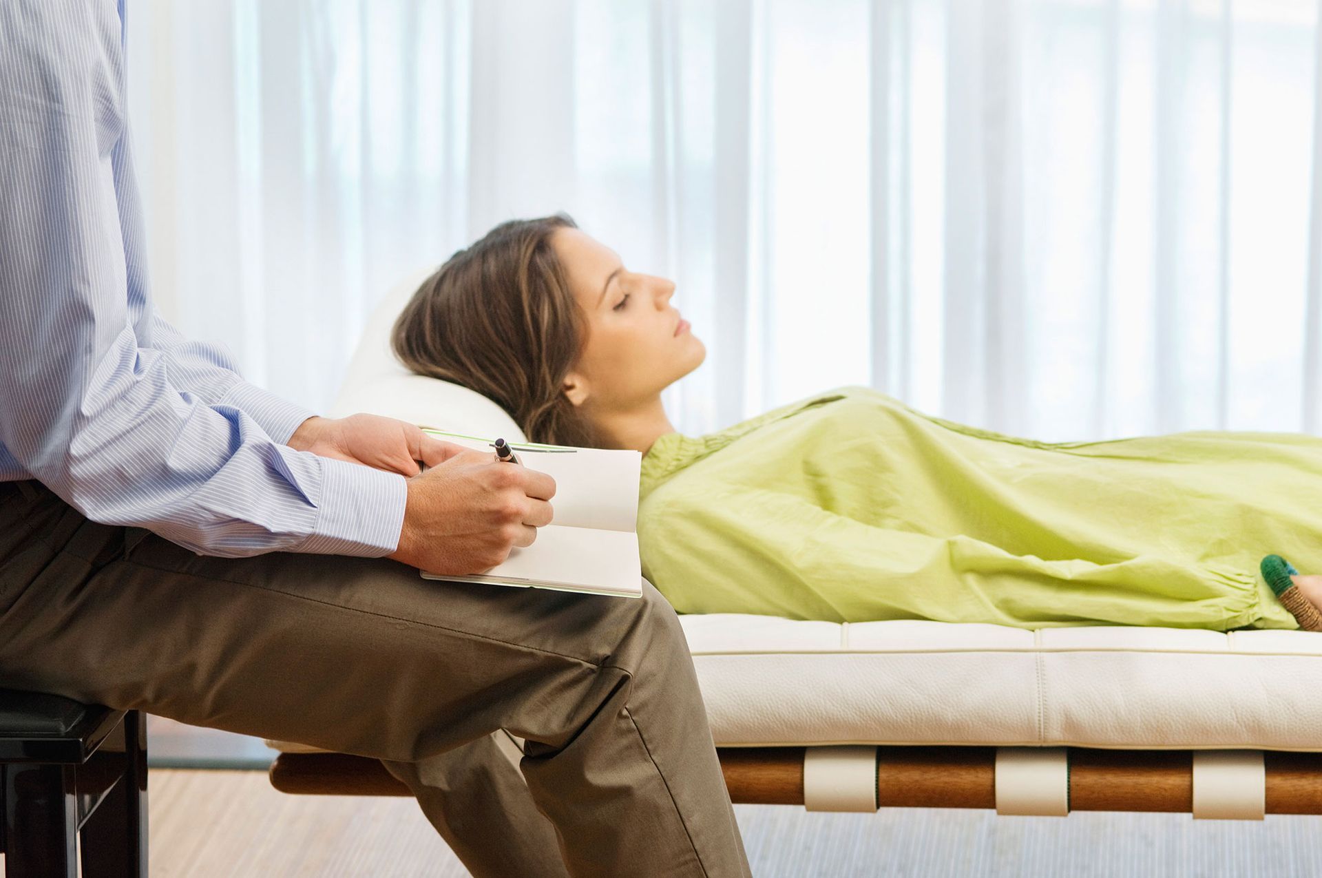 Woman lying on a therapy couch, eyes closed, with a person holding a notepad.