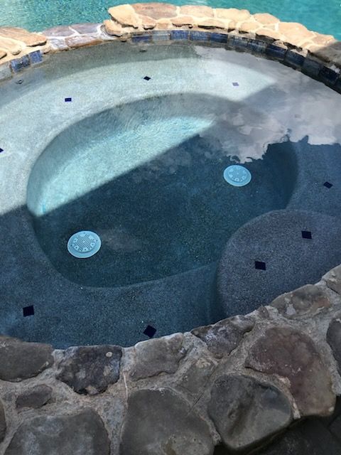 A hot tub surrounded by rocks next to a swimming pool