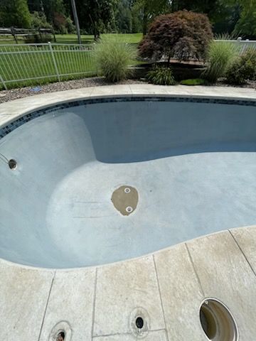 A large swimming pool with a fence around it and a tree in the background.
