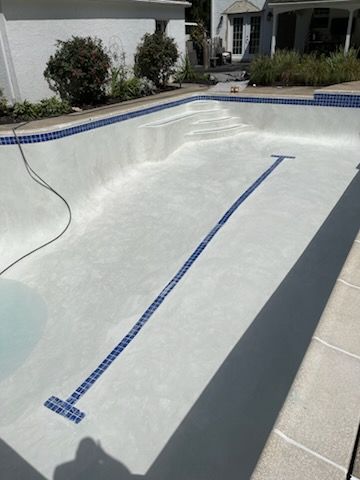 A large white swimming pool with blue tiles and a house in the background.