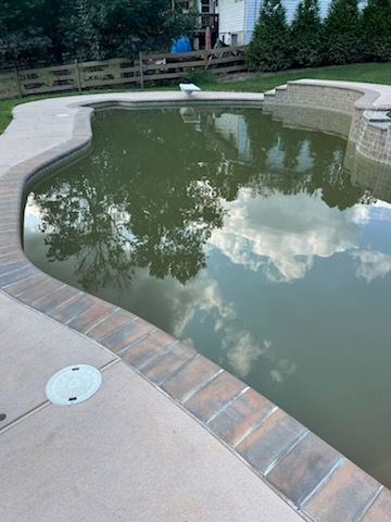 A swimming pool with a brick walkway surrounding it and trees reflected in the water.