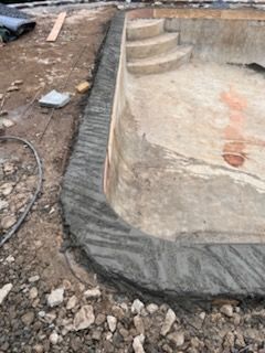 A swimming pool is being built in the dirt with stairs.