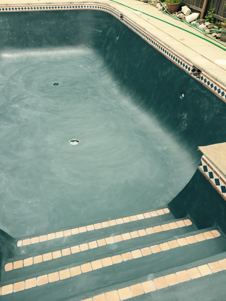 An empty swimming pool with stairs and a green hose.