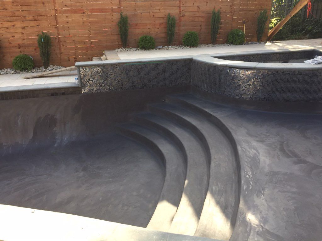 A swimming pool with stairs and a wooden fence in the background.