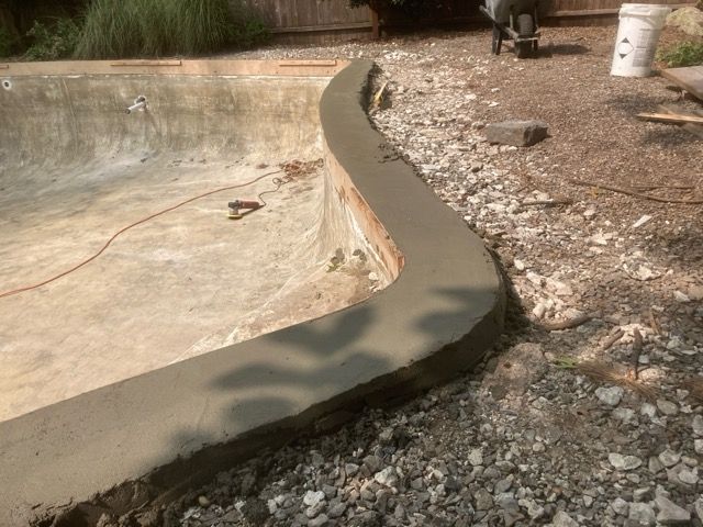 A concrete curb is being built around a pool.