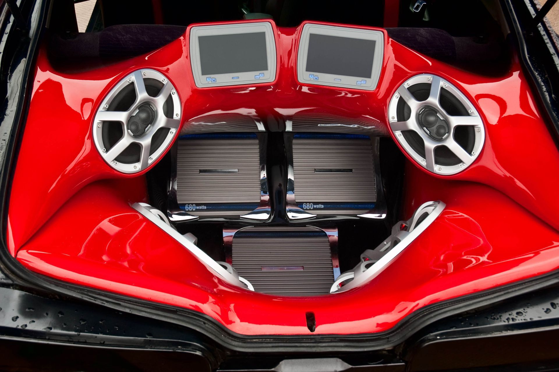 Custom red car trunk enclosure featuring two video screens, two speakers, and three metallic amplifiers.