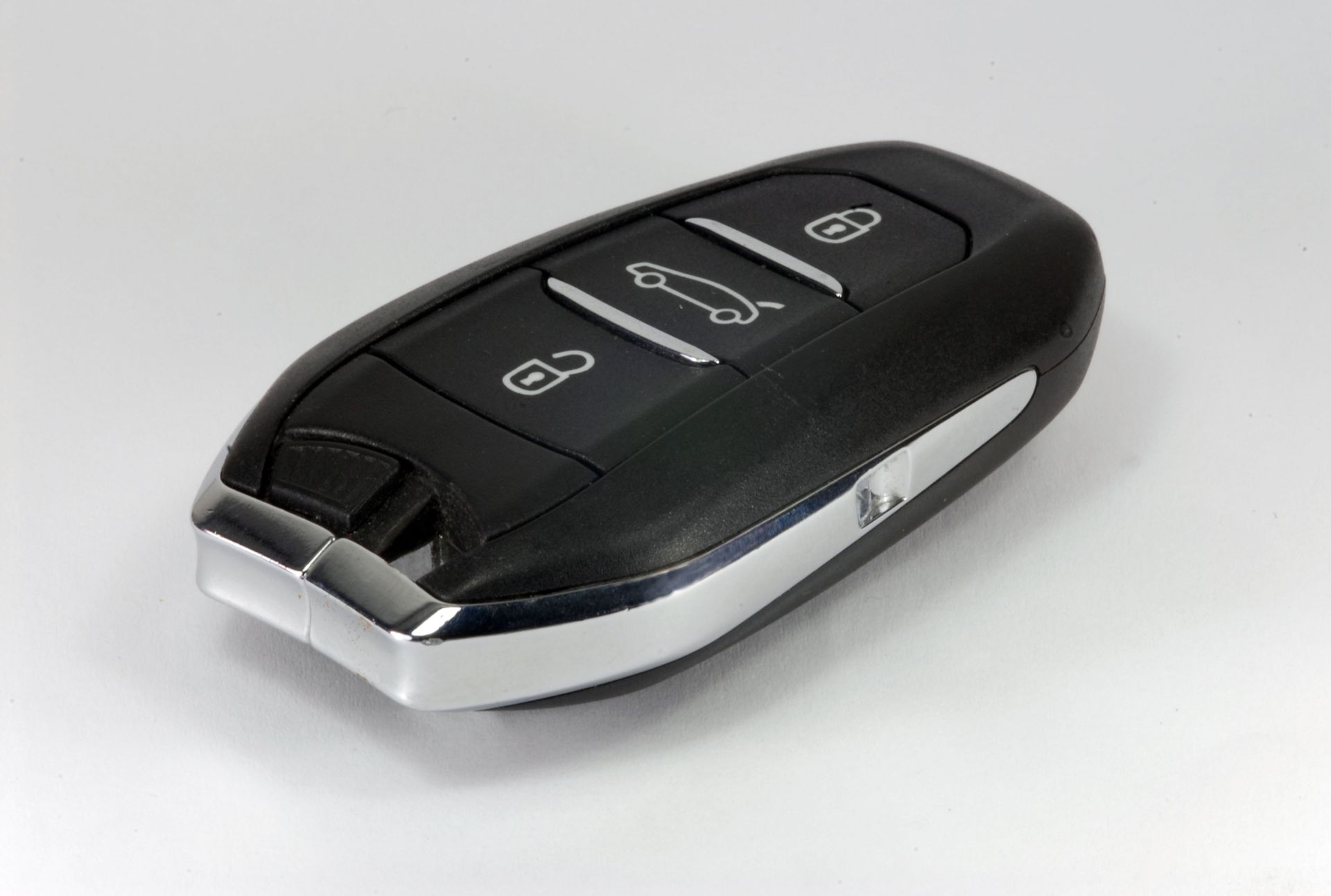 A black car key fob with silver accents and three buttons for locking, unlocking, and opening the trunk on a white background.