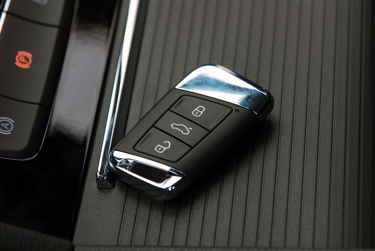 A modern car key fob with lock, unlock, and trunk buttons resting on a textured black vehicle center console.