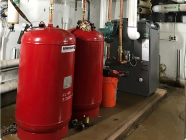 Two red Armstrong tanks and boiler in a utility room.