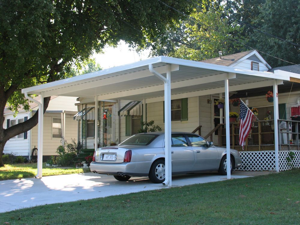 Car parked under a white carport in front of a house with an American flag.