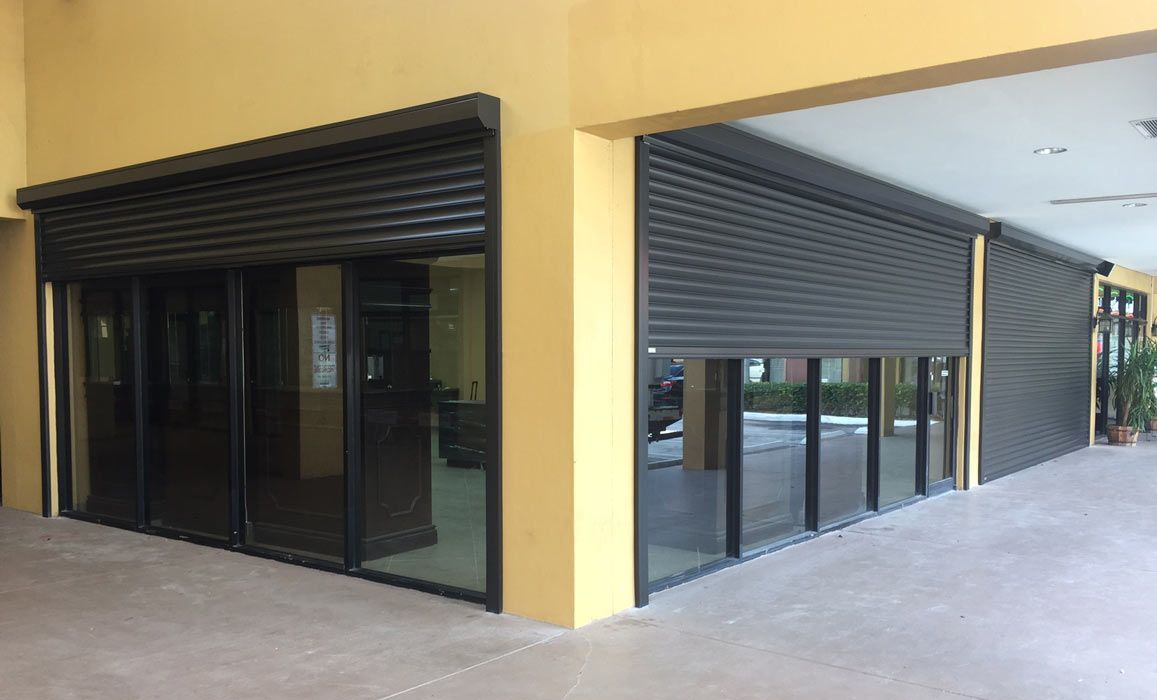 Exterior of building with black roller shutters over glass doors and windows; yellow walls.