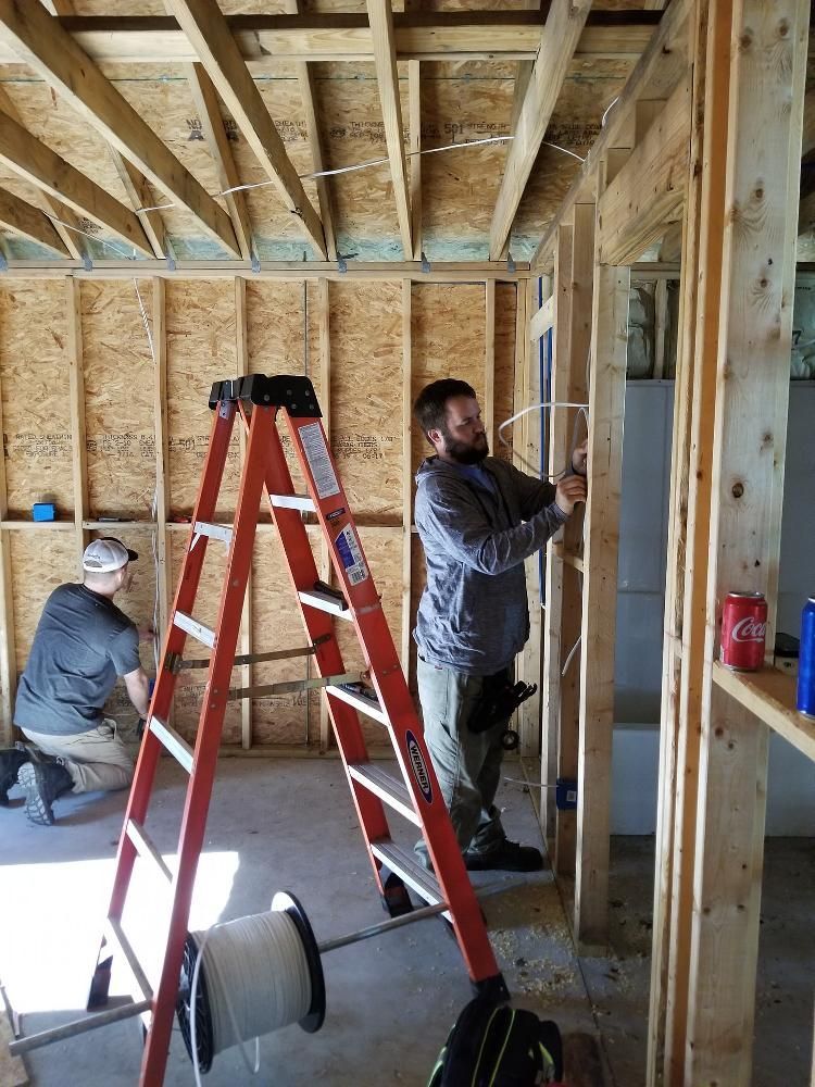 Two men are working on a house in a room with a ladder.