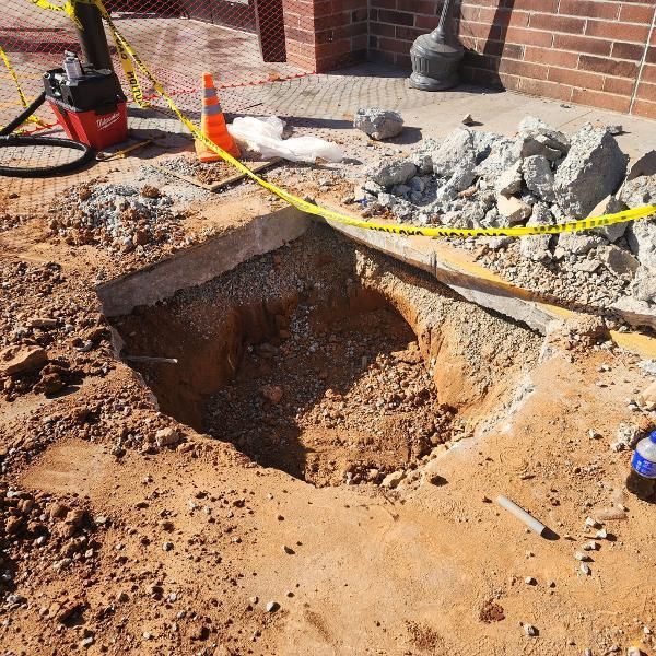 A hole in the ground with a vacuum cleaner in the background