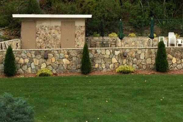 A stone wall surrounds a lush green lawn in a backyard.
