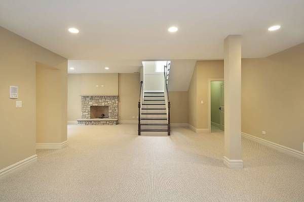An empty basement with stairs leading up to the second floor and a fireplace.