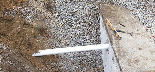 A white pipe is laying on the ground next to a hammer.