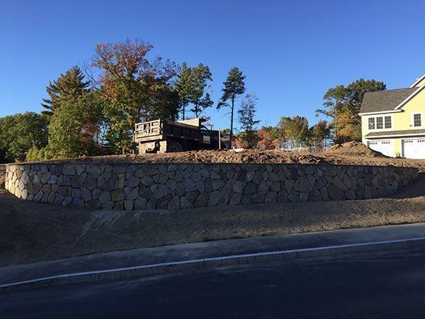 A large stone wall is surrounded by trees and a house.