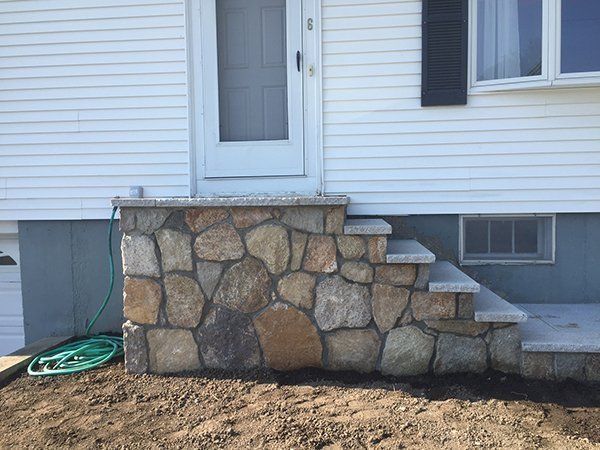 A stone wall with stairs leading up to the front door of a house.