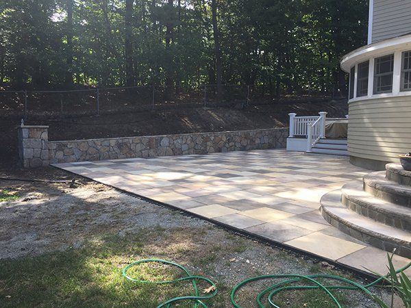 A patio with a stone wall and a hose in front of a house.