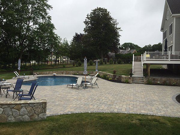 A large swimming pool is surrounded by chairs and umbrellas on a patio.