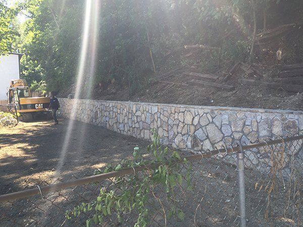 A bulldozer is driving down a dirt road next to a stone wall.