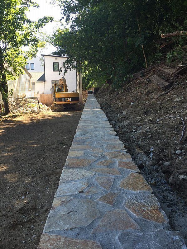 A cat excavator is parked next to a stone walkway