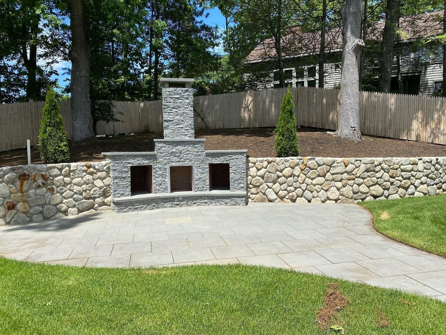 A stone fireplace is sitting in the middle of a lush green yard.