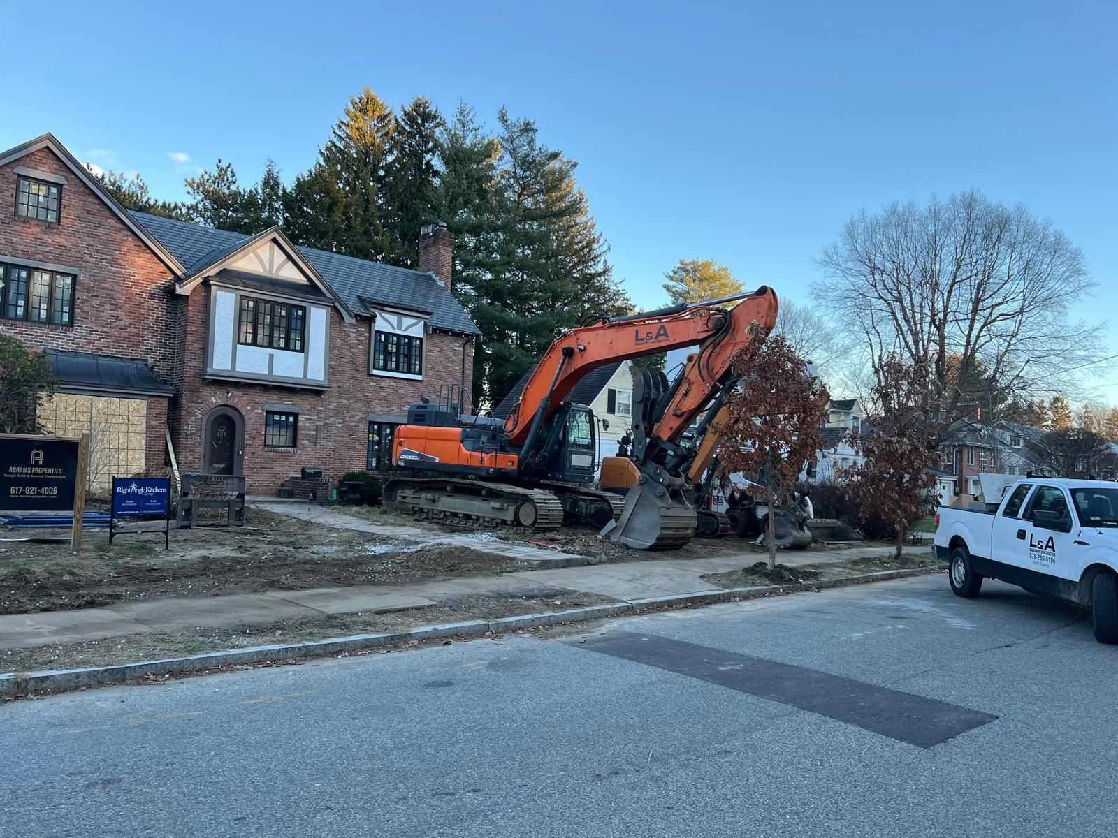 A large excavator is sitting in front of a brick house.