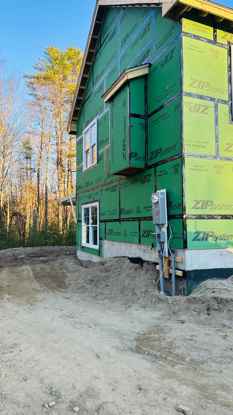 A house is being built in the woods and is covered in green insulation.