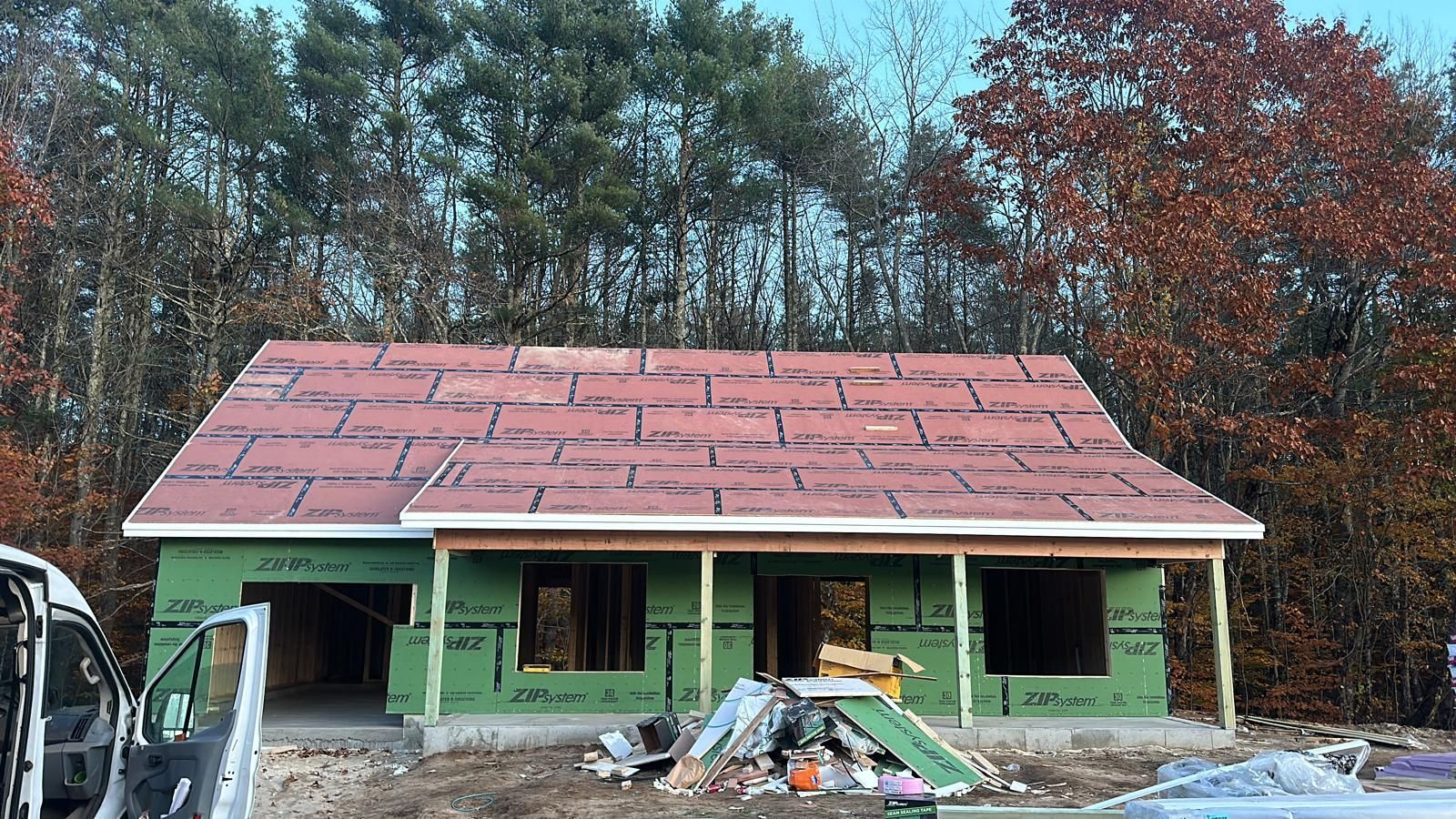 A house under construction with a red roof is surrounded by trees.