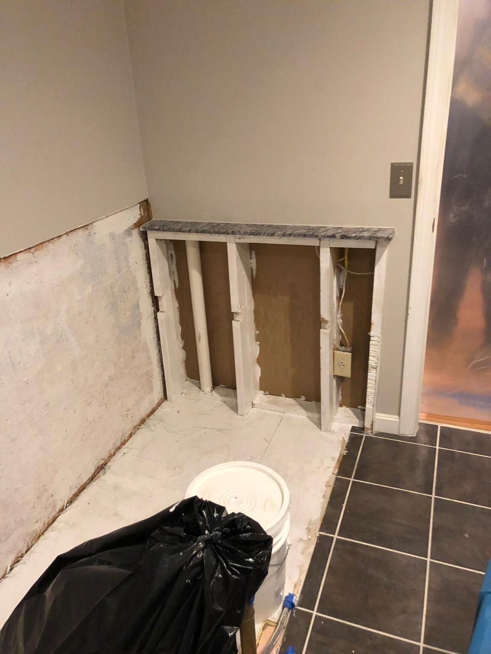A bathroom with a bucket of paint and a black bag on the floor.