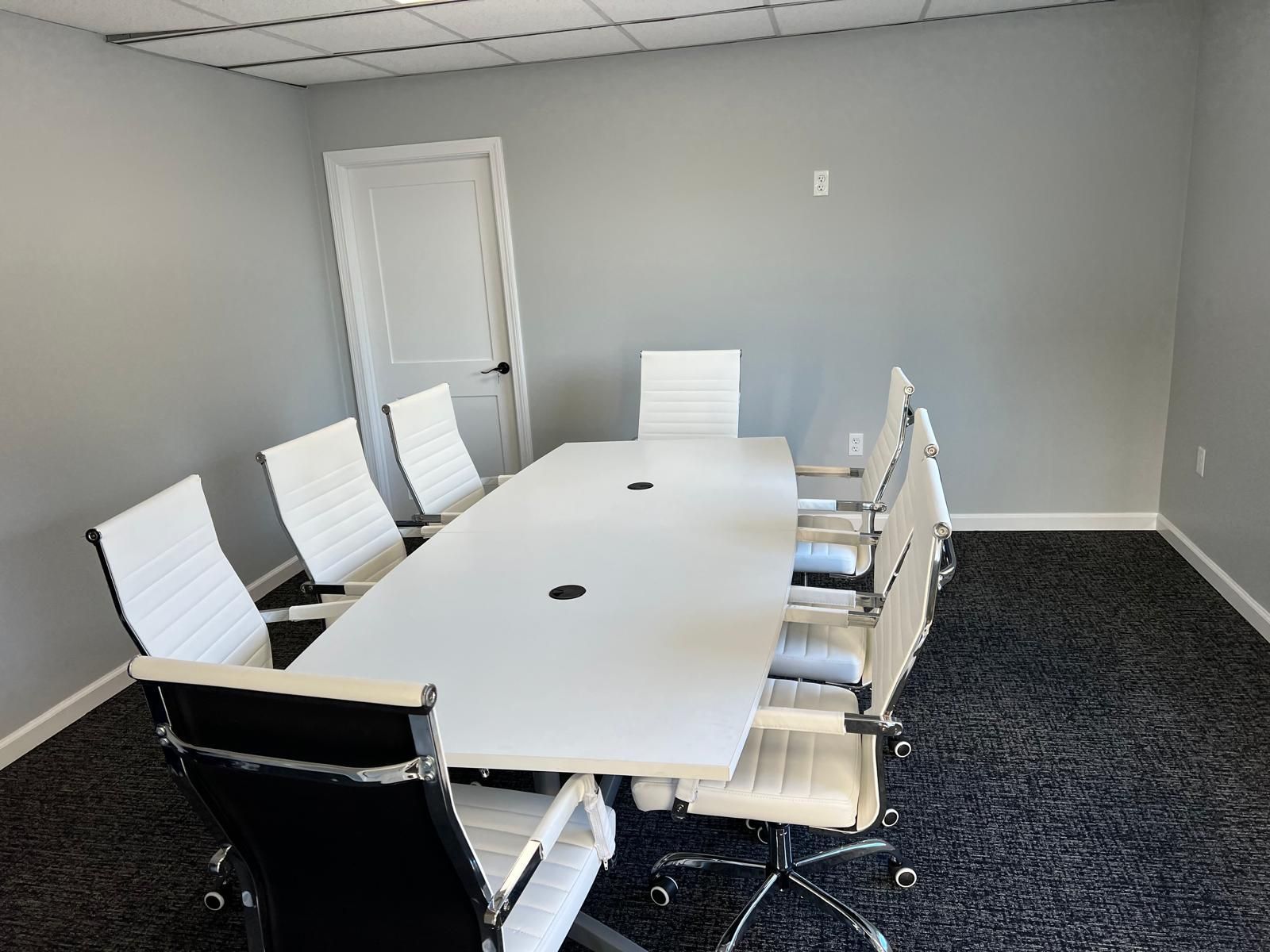 A conference room with a long white table and black chairs.