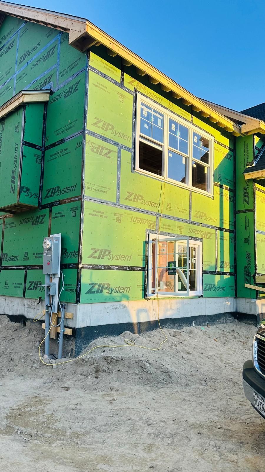 A house is being built with green insulation and a truck is parked in front of it.