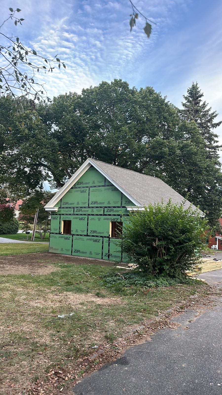 A small green house is being built next to a road.