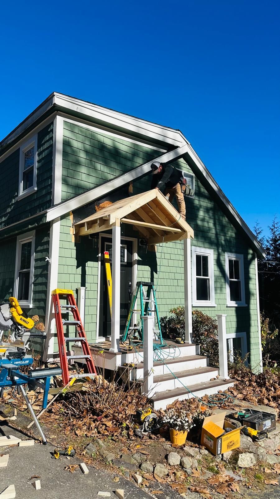 A green house with a porch being built on it.