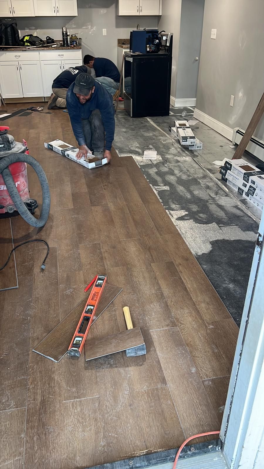 A man is installing a hardwood floor in a kitchen.