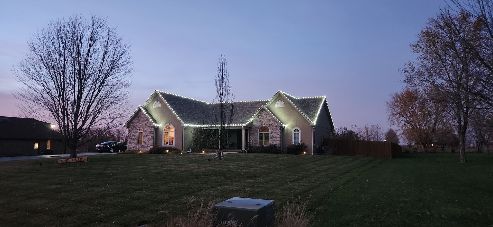 House with white Christmas lights outlining roof at dusk.