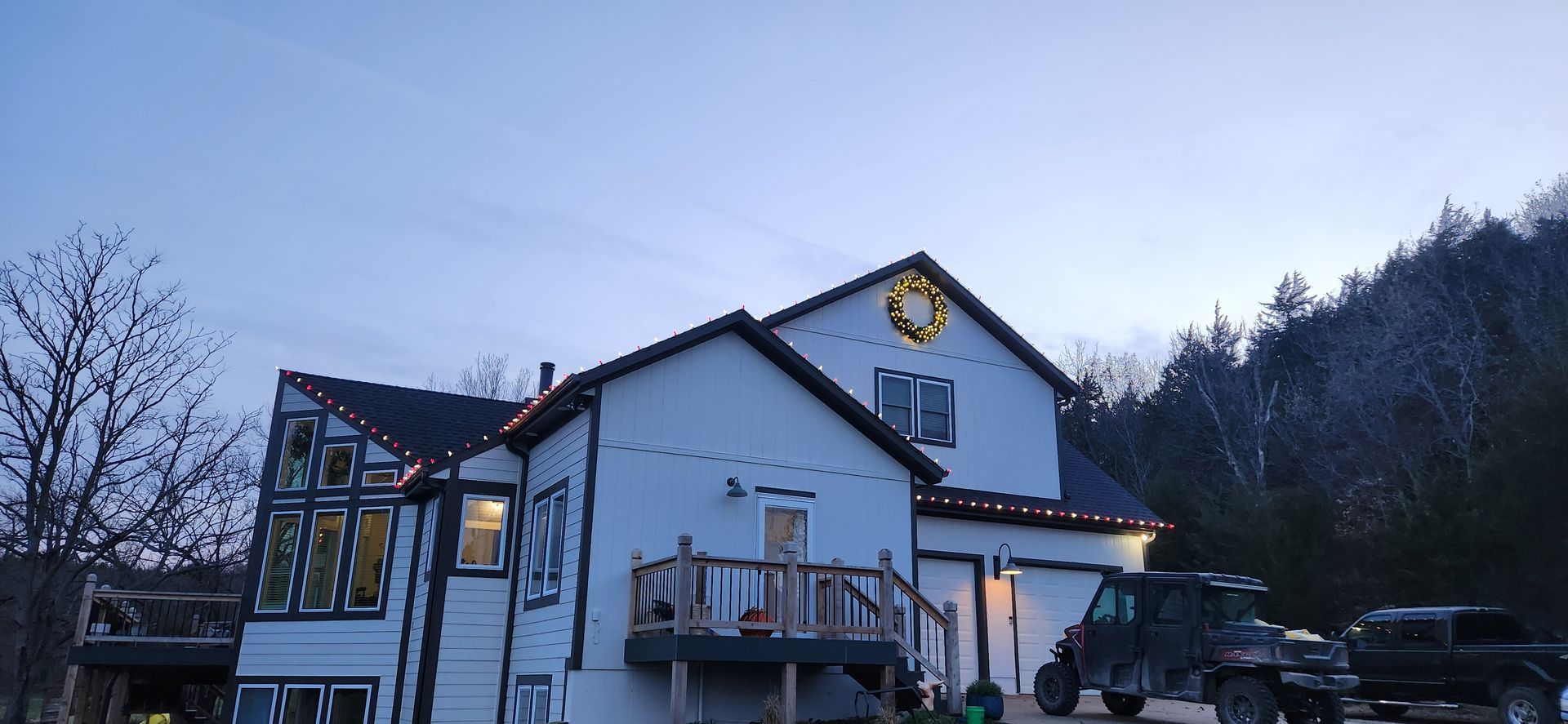 House at dusk with Christmas lights and vehicles in the driveway.