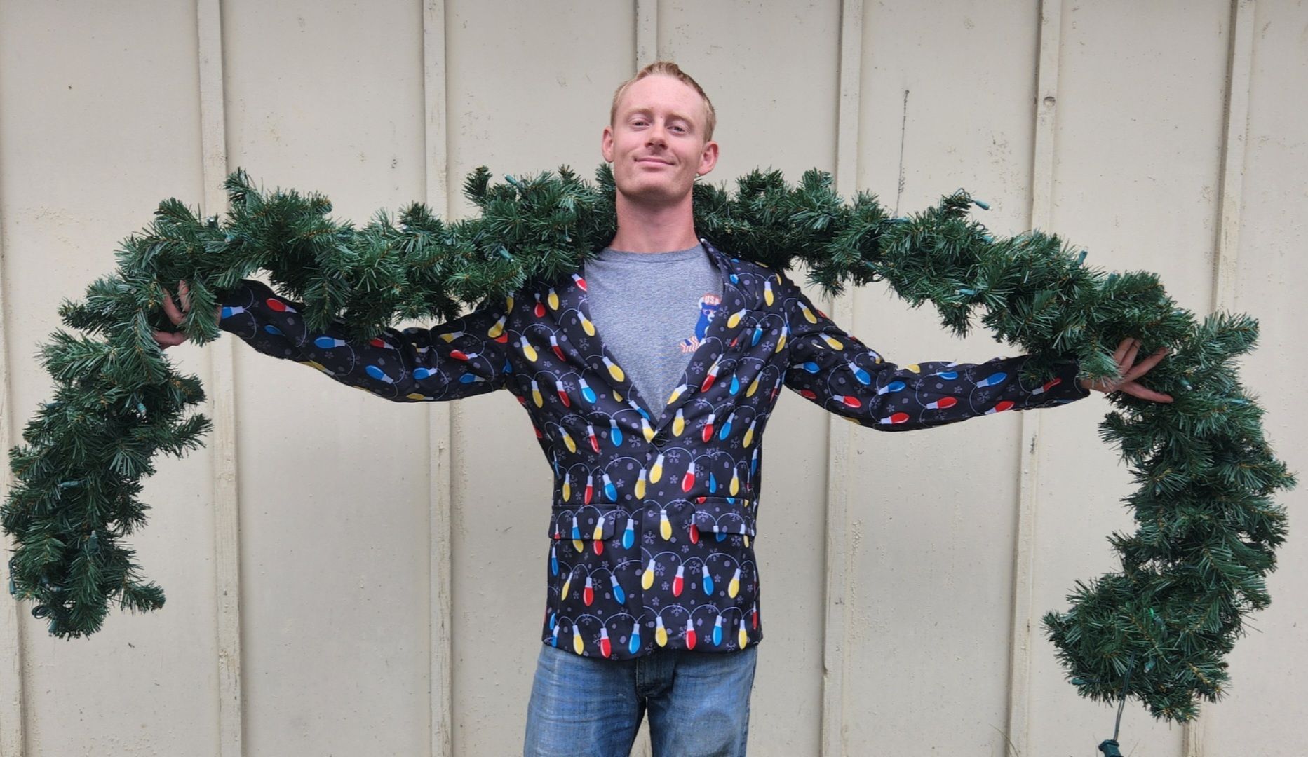 Man in Christmas light jacket holding a garland, smiling.