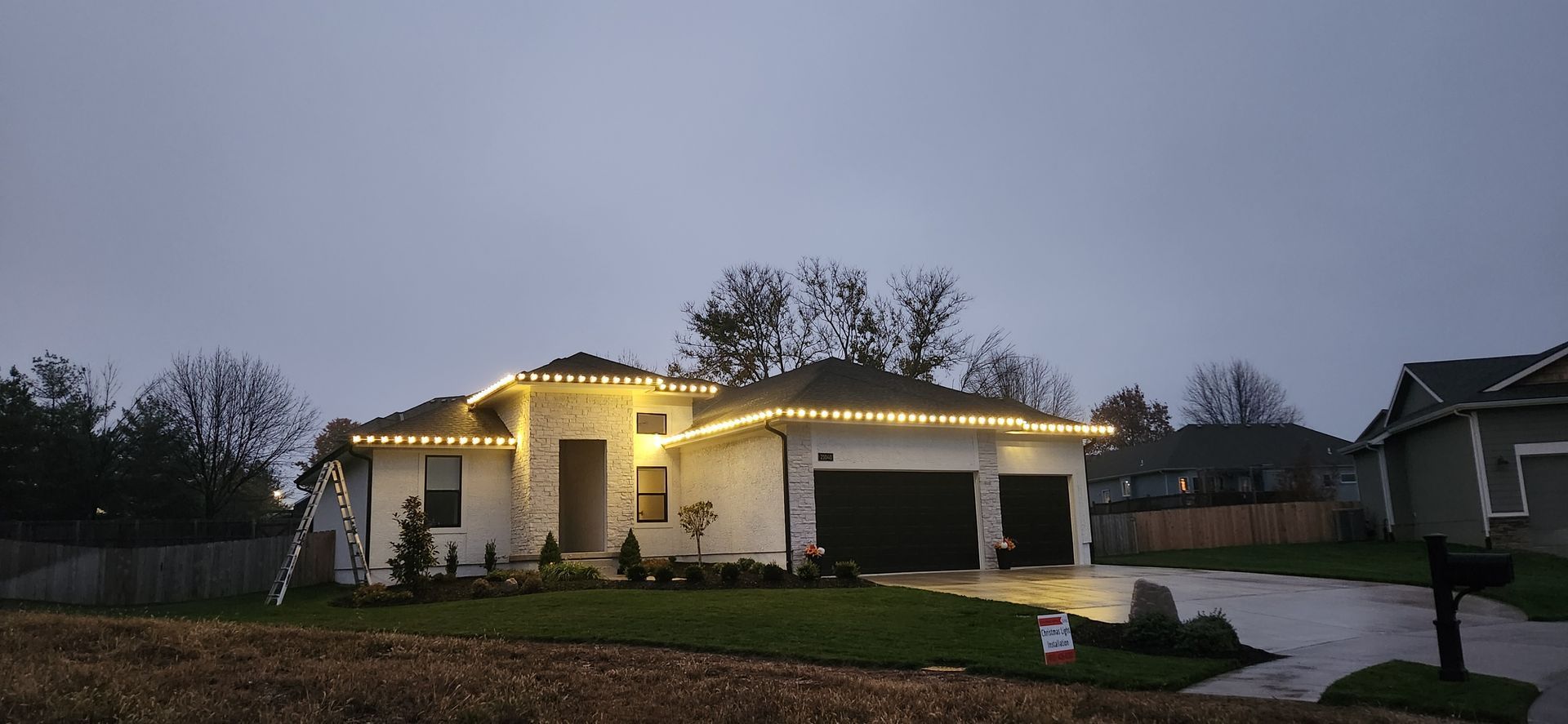 A white house with Christmas lights under a cloudy sky.