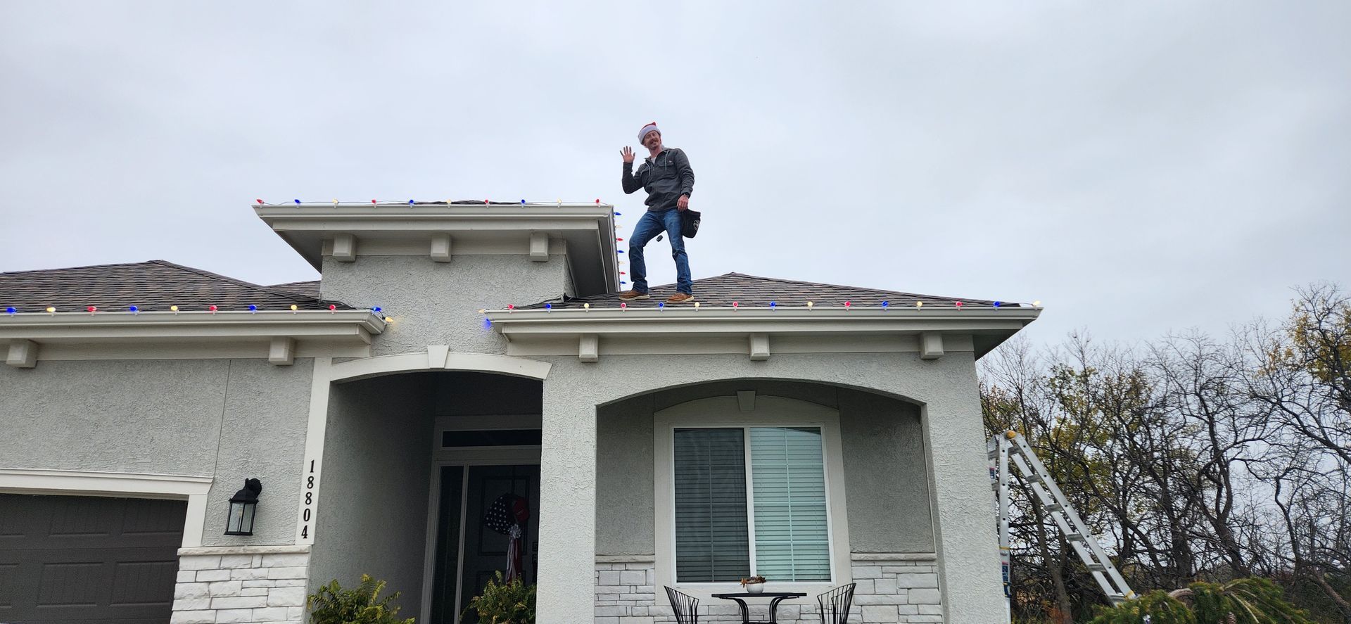 Man on a roof, giving a thumbs up. Residential house, cloudy day.