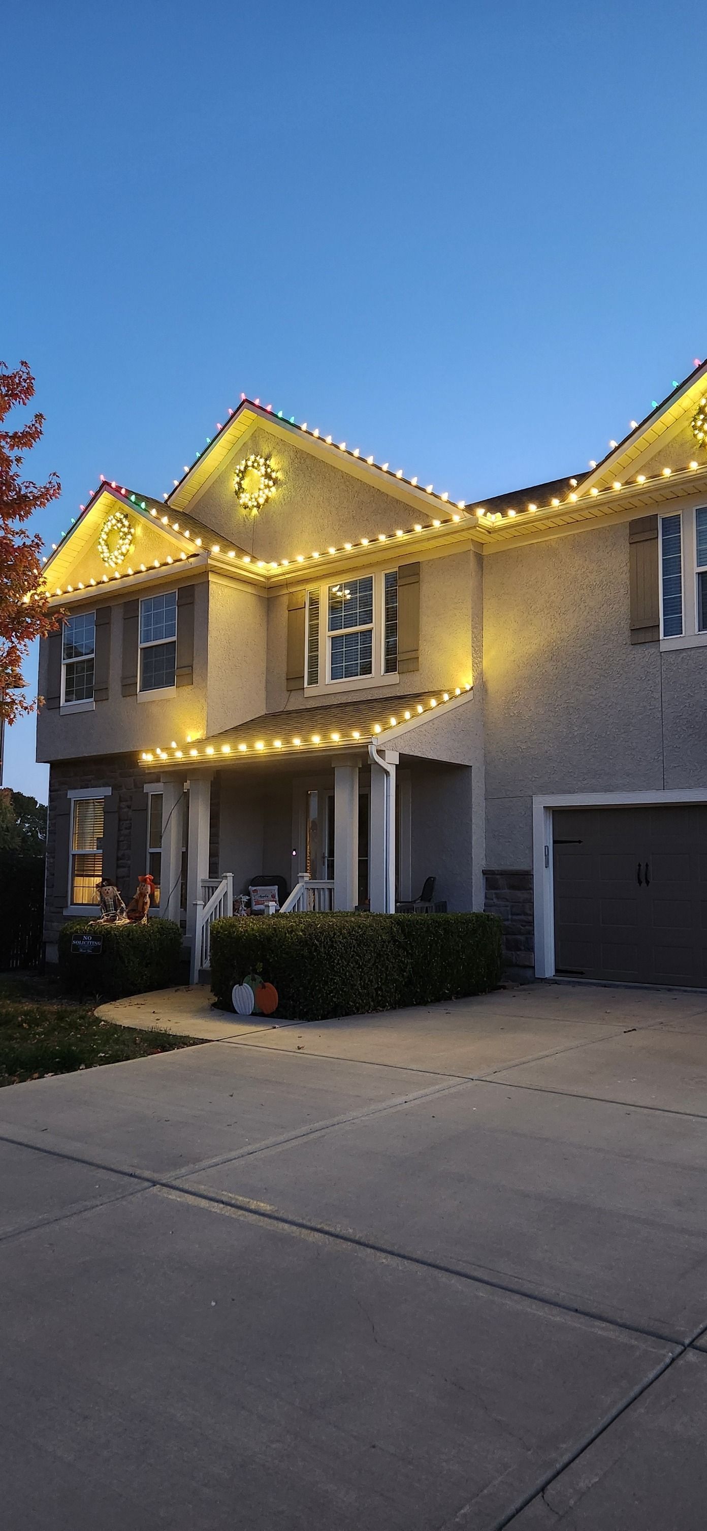 A two-story house with warm-toned Christmas lights against a dusk sky.