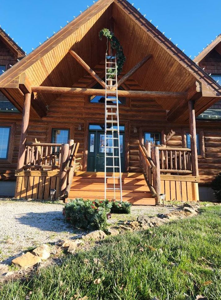 Ladder leaning against a log cabin, person decorating with greenery.