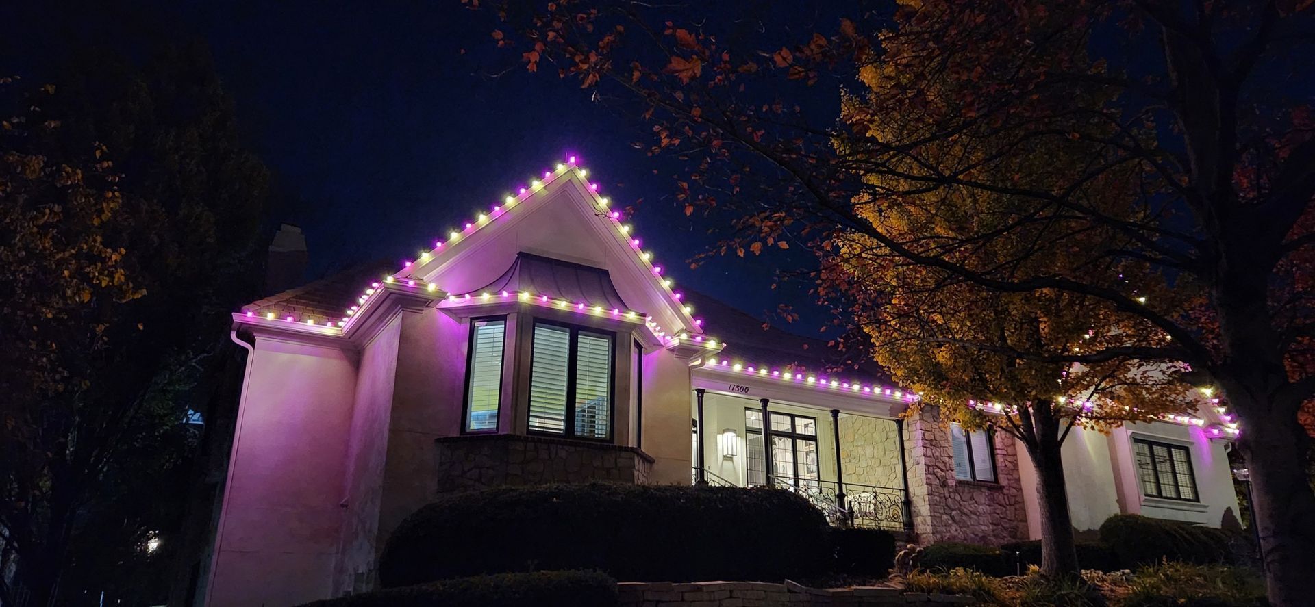 House with purple and white lights lining the roof at night.