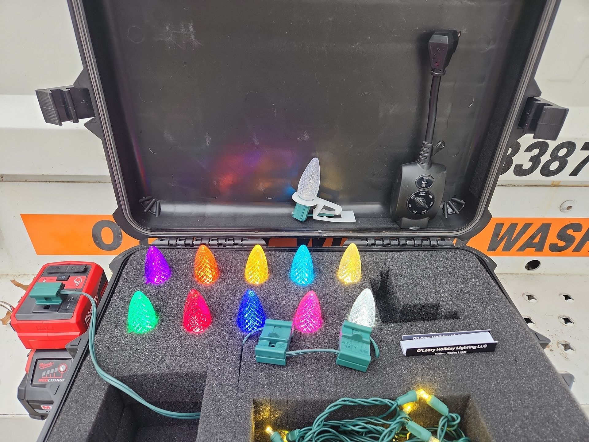Open black case with multi-colored C9 LED bulbs, battery pack, and a small black shovel.