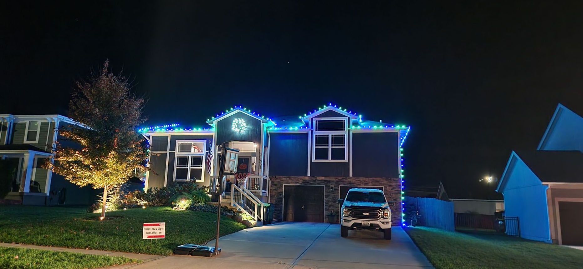 House with blue Christmas lights at night; car in the driveway.